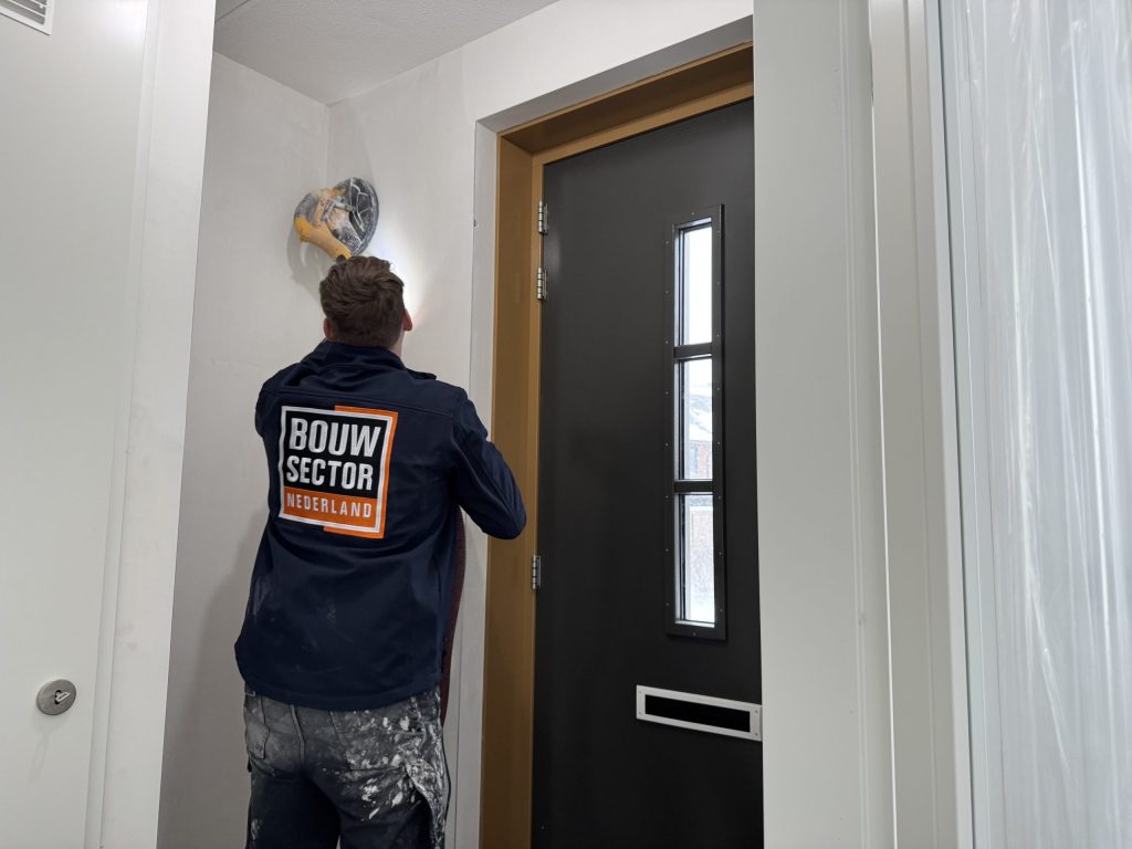 Vakman van Bouwsector Nederland schuurt de wand in een hal naast de voordeur